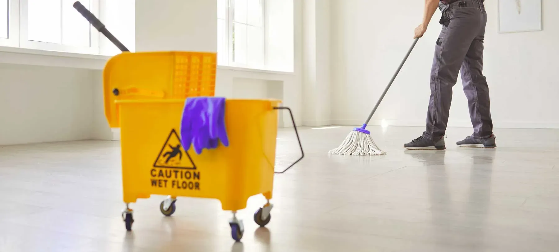 Cleaner mopping an empty room beside a yellow bucket during turnover cleaning