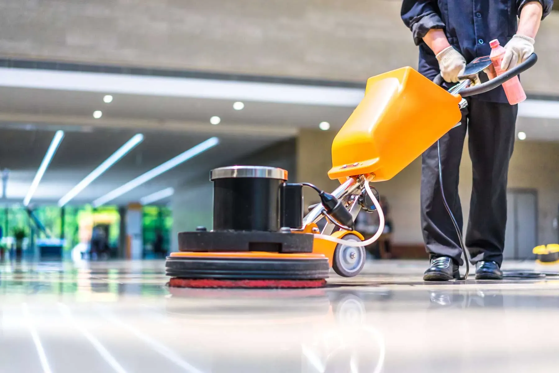 Cleaner operating a rotary floor machine on a glossy commercial floor